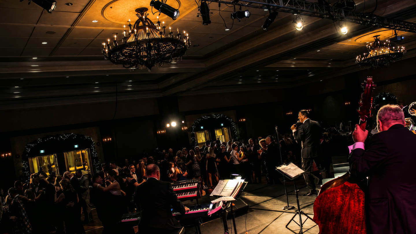 A chandeliered hotel ballroom during a gala — full dance floor, Barry Shaw and his band performing on stage